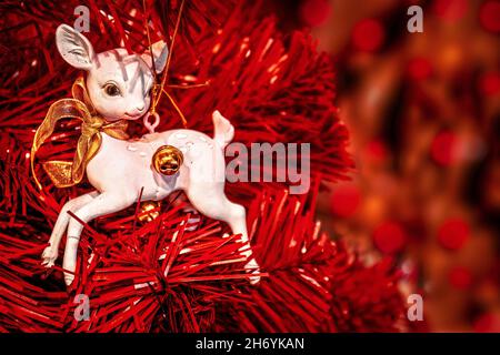 Ornamento di cervo bianco con arco d'oro su albero di Natale rosso a un bordo di cornice con sfondo bokeh - stanza per la copia. Foto Stock