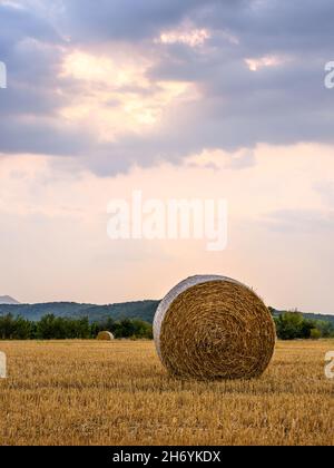 tramonto con gli ultimi raggi del sole che piercing le nuvole su un campo di grano raccolto con una balla di paglia in primo piano Foto Stock