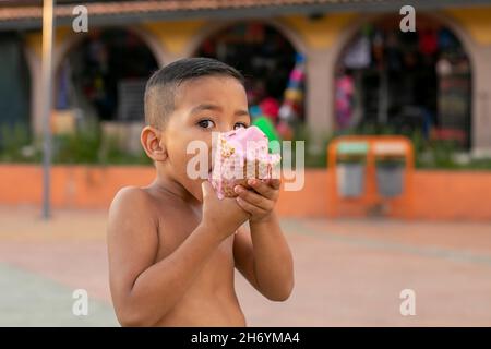 Allegro ragazzo ispanico che cammina in un parco senza una camicia e mangiare gelato Foto Stock