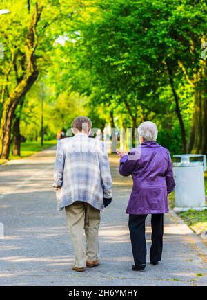 POZNAN, POLONIA - 02 maggio 2014: Un colpo verticale di una coppia anziana che cammina su un sentiero del parco nel distretto di Piastowskie a Poznan, Polonia Foto Stock