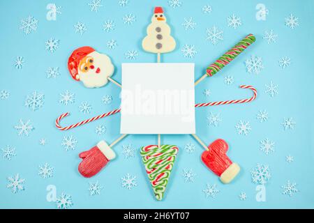 Caramelle natalizie a forma di pupazzo di neve, albero di natale, babbo natale, mitten e fiocchi di neve su sfondo blu. Lollipop, canna di caramelle. Disposizione piatta, vista dall'alto. Spazio di copia Foto Stock