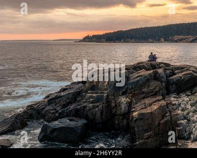 Acadia National Park, ME - USA - 14 ottobre 2021: Vista autunnale orizzontale di una coppia seduta su rocce godendo il tramonto a Otter Point ad Acadia Natio Foto Stock