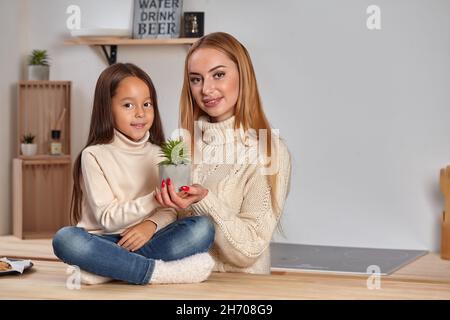 Bella mamma e la sua piccola figlia il fine settimana, seduto sul piano di lavoro, considerare un fiore in una pentola in cucina leggera Foto Stock