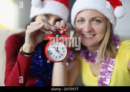 Le sorelle sorridono e tengono l'orologio retrò rosso con le frecce poste a mezzanotte Foto Stock