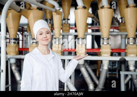 Concetto di industria alimentare moderna. Operatrice donna su fondo macchina elettrica mulino per la produzione di farina di grano. Foto Stock