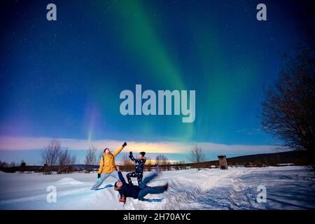 Compagnia di amici turisti guarda aurora luci nord notte a foresta, fuoco morbido. Foto Stock