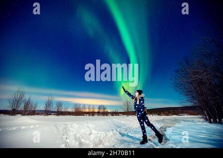 Donna turistica guarda aurora notte aurora luci nord a foresta, fuoco morbido. Foto Stock