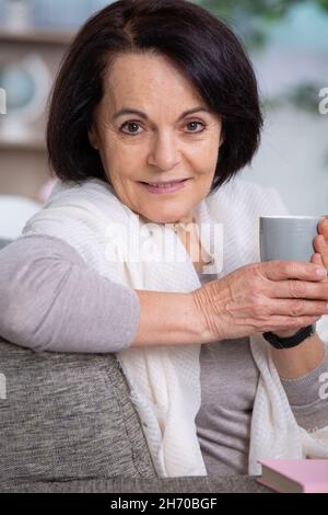 sorridente donna di mezza età che sorride il suo caffè seduto Foto Stock