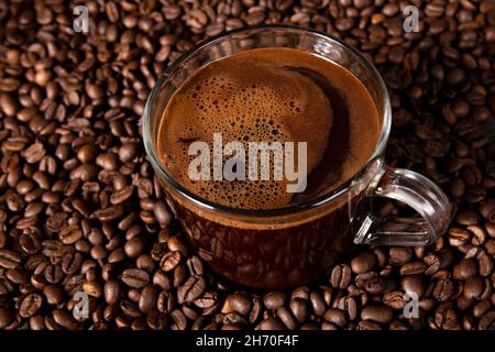 Tazza di caffè con caffè nero tradizionale appena fatto. Chicchi di caffè sullo sfondo. Messa a fuoco selettiva. Foto Stock