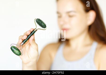 Ritratto sfocato di donna caucasica adulta, utilizzando jade naturale rullo di pietra per massaggio viso in giorno a casa. Spazio per la copia della vista frontale di cosmetica e bellezza. Foto Stock