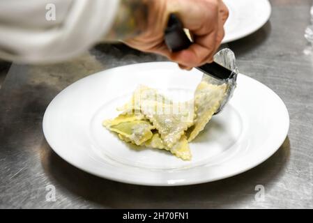 Coltivare il cuoco anonimo con cucchiaio da cucina mettendo appetitosi ravioli tradizionali italiani su piatto bianco mentre si serve il pasto al ristorante Foto Stock