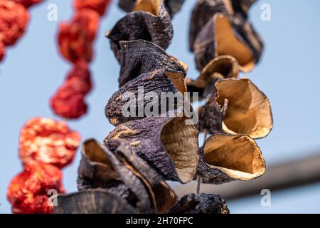 Melanzane secche e peperoncini secchi appesi sul mercato, ingredienti locali, closeup selettivo fuoco su sfondo sfocato. Foto Stock