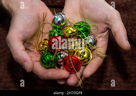 Campane gialle multicolore nelle mani degli uomini. Messa a fuoco selettiva. Sfondo scuro. Primo piano Foto Stock