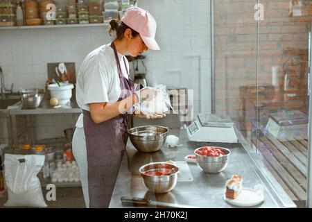 Il panettiere femminile savvolge il burro in piedi al banco di metallo con prodotti alimentari in negozio Foto Stock