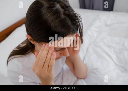 Infelice giovane donna premurosa che tiene le mani sulla fronte, sentendosi triste solo sedersi a letto da solo cercando di dormire pensando al problema, paure Foto Stock