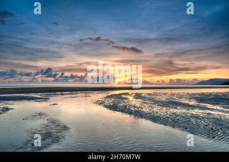 I canali di marea in uscita portano alla luce dorata del sole che sorge, mentre sembra che le nuvole si illuminino a Yule Point in QLD in Australia. Foto Stock