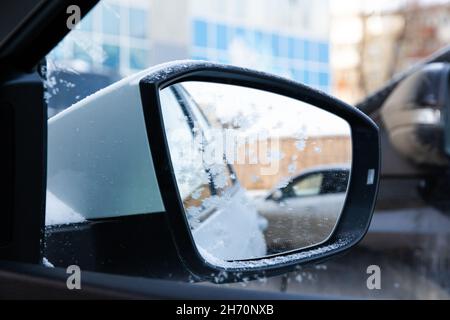 Specchio laterale di una nuova auto bianca coperta di neve con un riflesso coperto di gelo in una giornata soleggiata e gelata negli Urali. Messa a fuoco selettiva. Primo piano Foto Stock