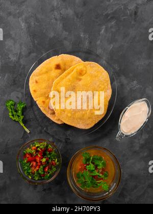 Pane piatto di mais fatto in casa cilantro verde salsa di pomodoro. Tortilla messicana Taco Quesadilla vegetale fatta a mano. Tradizionale indiano Makki ki roti pane top Foto Stock