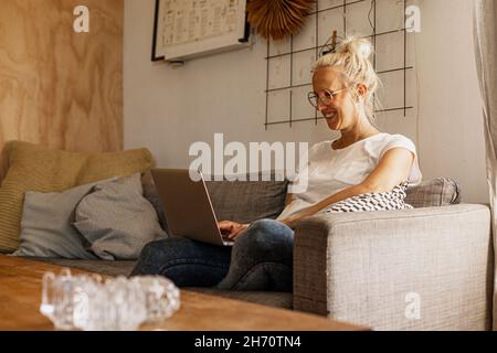 Donna sorridente con notebook sul divano Foto Stock