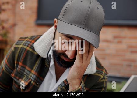 Uomo con barba e cappello da baseball a contatto con il viso Foto Stock