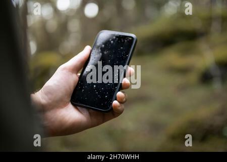 Tenere a mano lo smartphone bagnato nella foresta Foto Stock