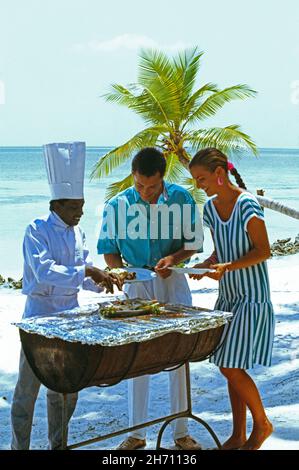 Maldive. Lo chef dell'hotel serve pranzo a giovani coppie sulla spiaggia. Foto Stock