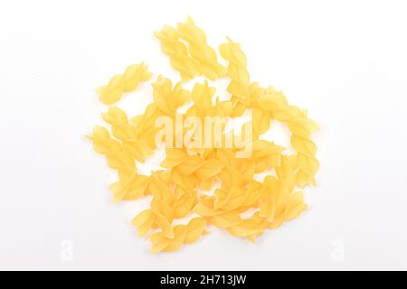 Un heap di pasta di Fusilli non cotta sparse su tavola bianca. Macaroni crudi e secchi. Cibo malsano e grasso. Cultura Italiana Foto Stock