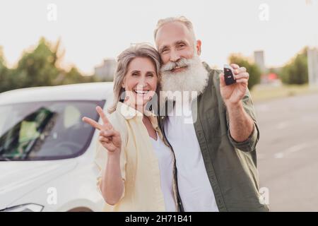 Foto di pensionato pensionato grigio capelli moglie marito anziani persone nuove chiavi auto v-segno fresco fuori fuori in città Foto Stock