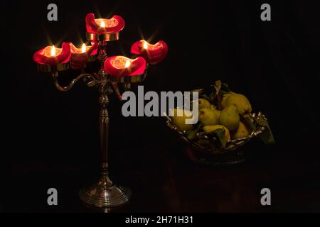 Candelabri con cadetti e cesto di frutta su un tavolo al buio. Foto Stock