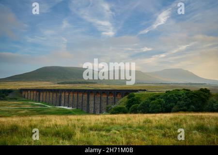 Campagna panoramica (storico punto di riferimento Ribblehead Viaduct in valle, luce del sole su archi, alto massiccio e colline) - North Yorkshire Dales, Inghilterra Regno Unito. Foto Stock
