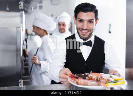 Cameriere con piatto di pesce in cucina al ristorante Foto Stock