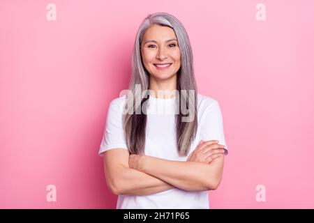 Ritratto fotografico di donna anziana che sorride con mani incrociate isolate su sfondo color rosa pastello Foto Stock