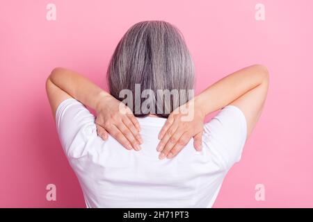Indietro vista ritratto di donna anziana che tocca le spalle ha ottenuto backache isolato su sfondo di colore rosa pastello Foto Stock