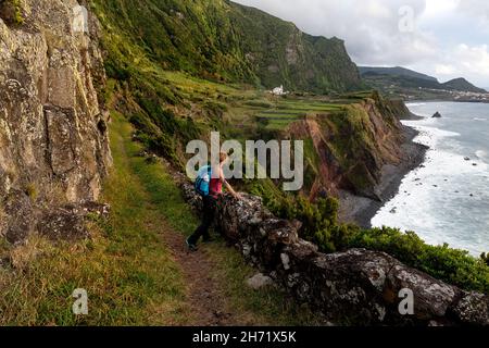 Donna che guarda in lontananza mentre si fa un'escursione su alte scogliere con una splendida vista su Faja Grande, l'isola di Flores, Azzorre, Portogallo Foto Stock