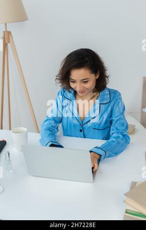 brunette giovane freelance che utilizza il computer portatile vicino a tazza e libri Foto Stock