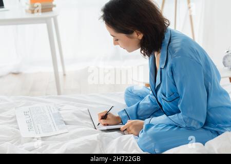 giovane donna che scrive nel taccuino vicino al giornale sul letto Foto Stock