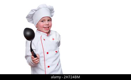 Divertente bambino sotto forma di uno chef con un cappello, sorride divertente, tiene un mestolo con un cucchiaio, guarda la macchina fotografica. Il concetto di ristorante o bar, Foto Stock