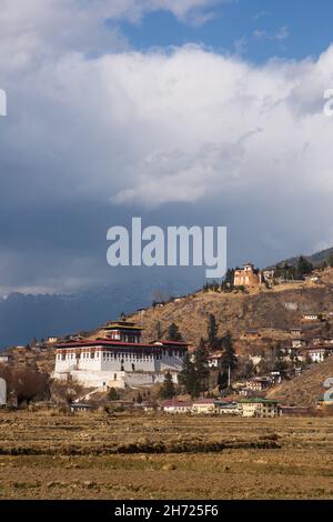 Il Paro Rinchen Pung Dzong e la torre di avvistamento Ta Dzong attraverso campi di riso arati a Paro, Bhutan. Foto Stock