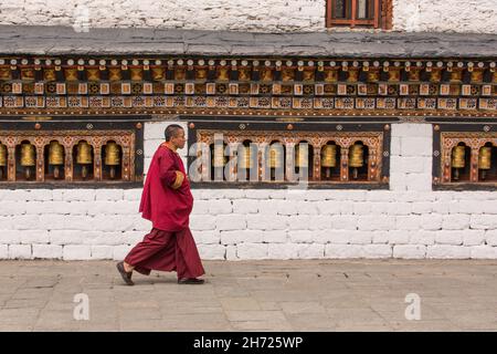 Un monaco buddista passa davanti a un muro di ruote di preghiera in un dochey o cortile nel Thimphu Dzong a Thimphu, Bhutan. Foto Stock