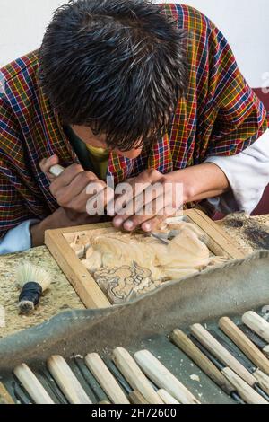 Un giovane uomo carve un leone di neve in legno nella Scuola Nazionale per le Arti Thirsteen a Thimphu, Bhutan. Foto Stock