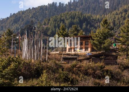 Una tradizionale fattoria bhutanese nel villaggio di Hongtsho, Bhutan. Di fronte vi sono un gruppo di bandiere di preghiera. Foto Stock