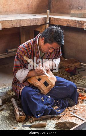 Un carver di legno che fa una maschera di legno nella scuola nazionale per le tredici arti in Bhutan. Foto Stock