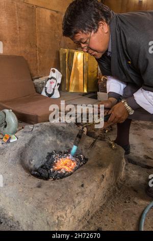 Un istruttore presso l'Istituto Nazionale delle tredici Arti riscalda il nastro per la produzione di gioielli con una torcia a soffiante. Thimphu, Bhutan. Foto Stock