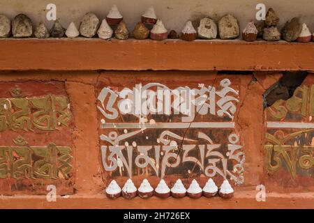 Sceneggiatura tibetana e tsatas su un muro al monastero di Dechen Phodrang a Thimphu, Bhutan. Foto Stock