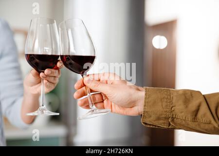 Primo piano di coppia bere vino rosso in cucina a casa, tostatura Foto Stock