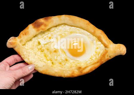 Il piatto nazionale georgiano è il khachapuri adjariano. Mano che tiene aperto formaggio a forma di barca e torta di uova isolato su sfondo nero, primo piano. Nazionale c Foto Stock