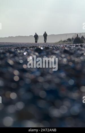 Due persone a piedi sulla spiaggia al tramonto in inverno con primo piano sfocato, Avon Beach Christchurch Regno Unito Foto Stock