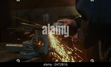 Primo piano utilizzare una macchina per il taglio di metalli o ferro e smerigliare i metalli su pezzi di ricambio in acciaio in officina Foto Stock