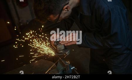 Primo piano giovane uomo fabbro utilizzare ferro o metallo taglio macchina e lui metallo rettifica su acciaio pezzo di ricambio in officina Foto Stock