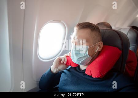 Il passeggero maschile dell'aereo ascolta la musica e gode di un cuscino  per dormire in sedia. Concetto di viaggio con maschera di sicurezza Foto  stock - Alamy